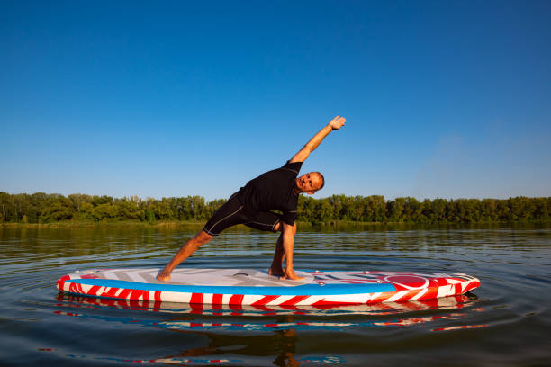 Man practicing yoga on a SUP board during sunset stock photo
