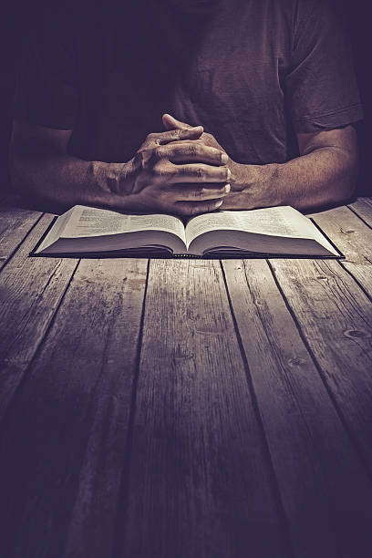 Man praying on a wooden table with an open Bible stock photo