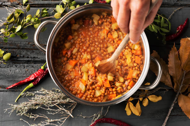 man preparing a vegetarian lentil stew high angle shot of a young caucasian man stirring a lentil stew, with a wooden spoon, in a stainless steel cooking pan placed on a gray rustic wooden table lentil stock pictures, royalty-free photos & images