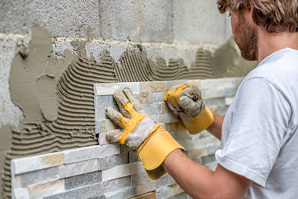 Man pressing ornamental tile into a glue on a wall stock photo
