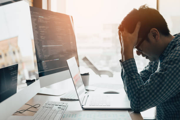 Man programmers are stressed and hand holding head with headache at the office while working analyzing on desk in code at office room. stock photo