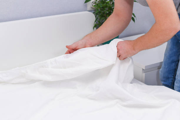 A man puts an elasticated sheet on mattress. Change of bed linen. stock photo