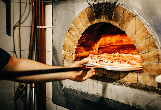 uomo che mette la pizza in forno - made in italy foto e immagini stock