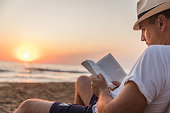 istock Man reading a book at the beach 1326850800