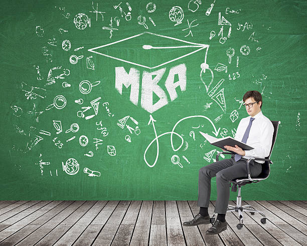 Man reading a book businessman sitting on a castor chair and reading a book,  science icons and 'MBA' drawn on the green blackboard behind him. MBA and the book connected. Concept of studying MBA stock pictures, royalty-free photos & images