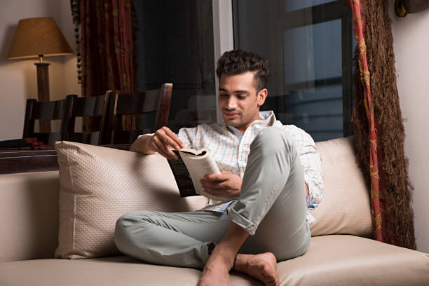 uomo che legge libro a casa - immagine di repertorio - accavallare le gambe foto e immagini stock