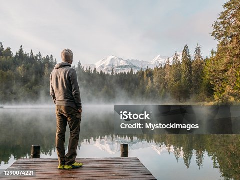 istock Man relax on wooden pier, looks out across lake 1290074221
