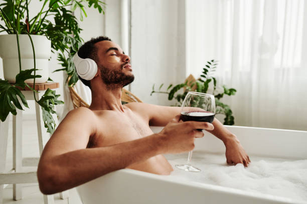 Man relaxing in bath with glass of wine stock photo