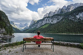 istock Man relaxing on bench in front of Dachstein Mountains reflected in Gosau lake, Austria 1329500649