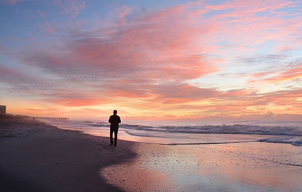 Man relaxing on the beach at sunrise. Man walking on the beautiful  beach at sunrise. Atlantic Beach, North Carolina. north carolina beach stock pictures, royalty-free photos & images
