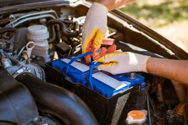 A man removes a battery from under the hood of a car. Battery replacement and repair stock photo