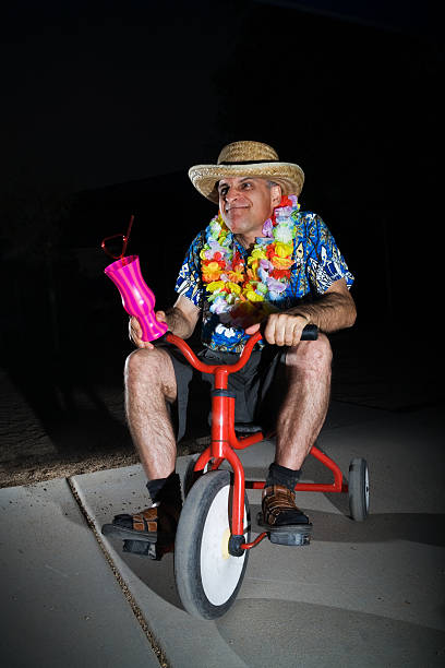 Man Riding Tricycle a mid-40 year old man wearing Hawaiian lei, shirt and hat riding a tricycle, holding his tropical drink and acting silly. adult tricycle stock pictures, royalty-free photos & images