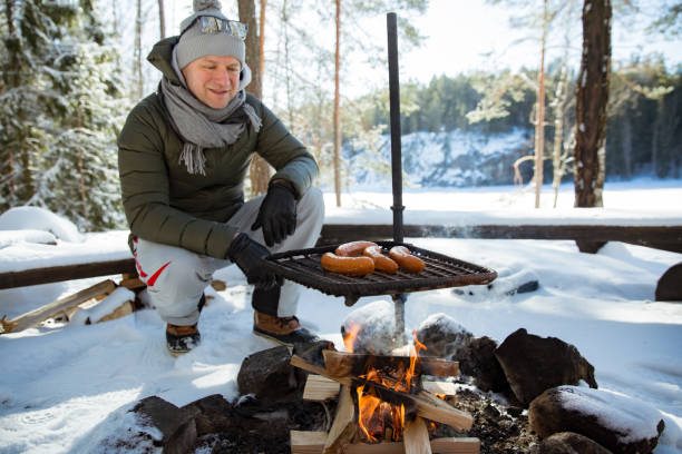 Man roasting sausages on campfire in forest by the lake stock photo