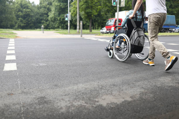 man rolls woman in wheelchair across the road. - wheelchair street imagens e fotografias de stock