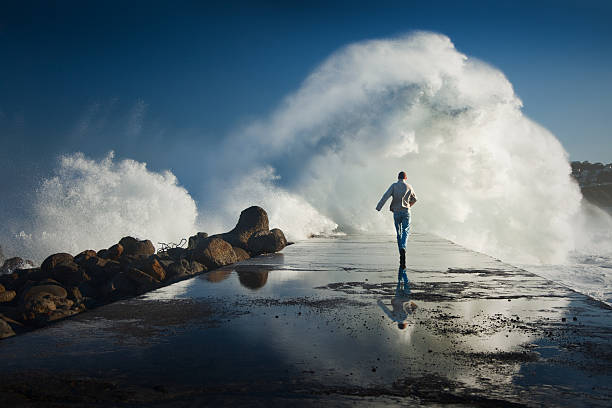 Man running away to dangerous ocean waves stock photo