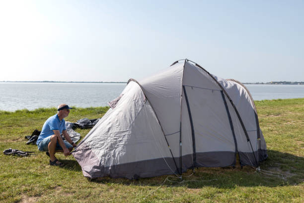 man setting up a tent at the waterline stock photo