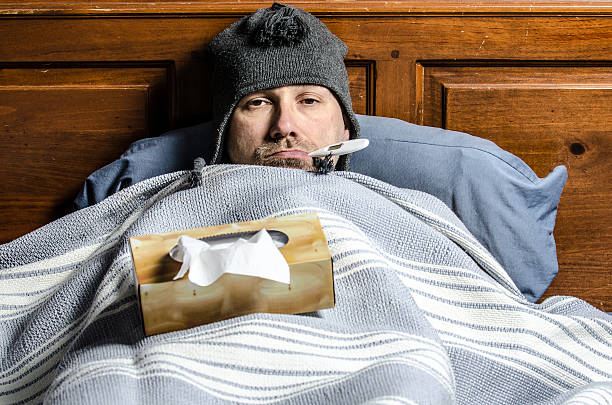 man sick in bed with a thermometer in his mouth stock photo