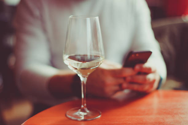 Man sitting at the table with a glass of white sparkling wine and mobile phone  - focus on glass stock photo