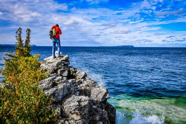 Man sitting on a coastline Man photographs a wave crashing against the Peninsula cliff face bruce peninsula stock pictures, royalty-free photos & images