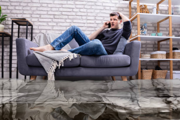 Man Sitting On Sofa Calling To Plumber Flooded Floor From Water Leakage In Front Of Man Sitting On Sofa Calling To Plumber flood photos stock pictures, royalty-free photos & images