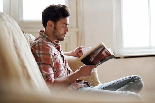 Man sitting on sofa reading a book in a cozy loft apartment