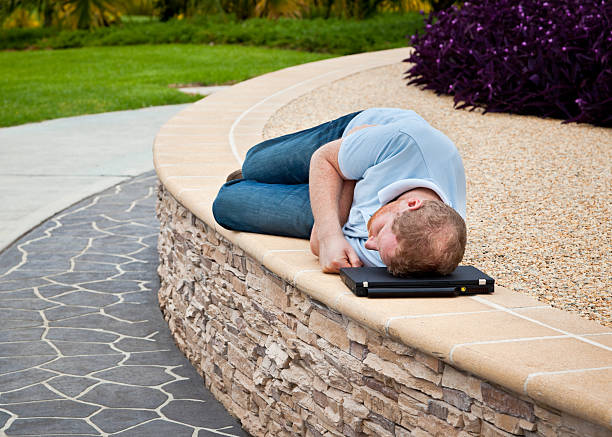 Man sleeping in a park with laptop as pillow stock photo