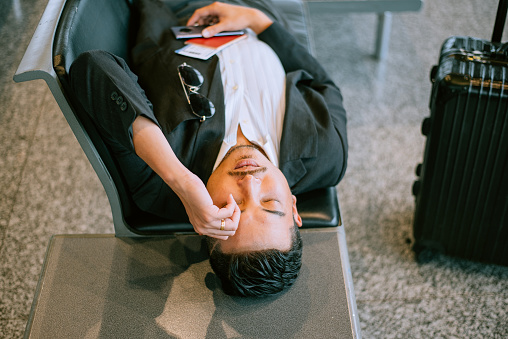 Man sleeping with his luggage lean aside airport terminal building interior