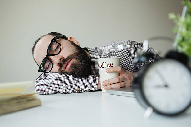 Man sleeps on office table over laptop with coffee stock photo