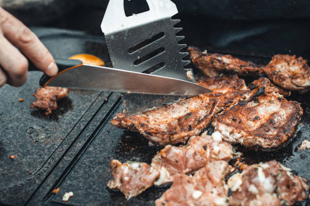 Man slices a pork neck, fragrant and richly seasoned with basil, pepper, salt and other herbs, which is fried on a granite slab over an open fire. Food preparation at a family event. Barbecue season stock photo