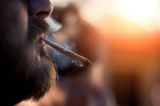 Man smoking marijuana cigarette outside on sunset stock photo
