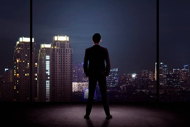 man standing in his office looking at the city - pakjesavond stockfoto's en -beelden