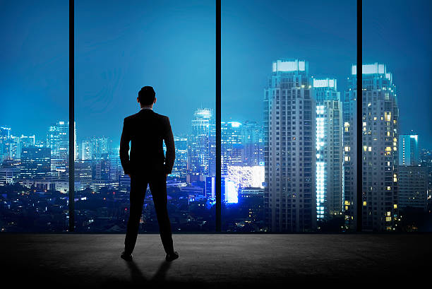 man standing in his office looking at the city - pakjesavond stockfoto's en -beelden