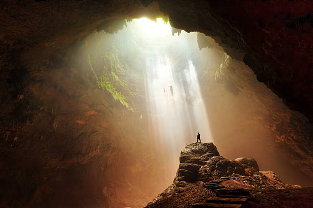 Man Standing on rock underground cave light yogyakarta indonesia A man standing on stone undergound cave. Ray of Light of heaven was taken in Jomblang Cave,  a vertical cave with dense ancient forest below. A 300 meter alley with its beautiful natural ornament a place where can see light from heaven. cave photos stock pictures, royalty-free photos & images