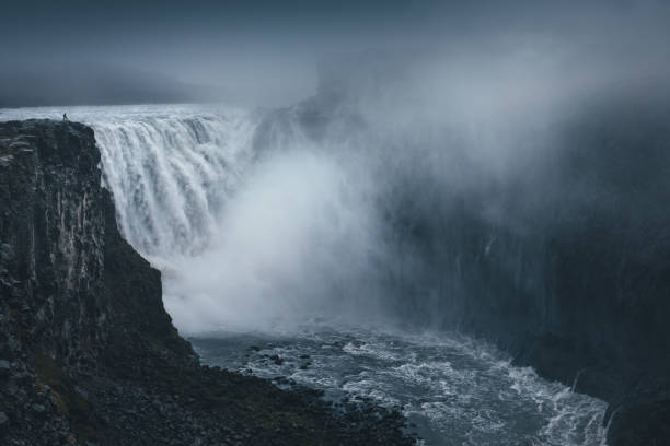 Man Standing On Top Of Dettifoss Man standing on top of majestic Dettifoss waterfall in north Iceland. iceland dettifoss stock pictures, royalty-free photos & images