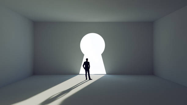 Man stands before a key decision and faces a wall with giant key hole stock photo