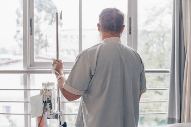 A man stands in a hospital ward and looks out the window. Dropper in a mans hand in a hospital  infusion therapy stock pictures, royalty-free photos & images