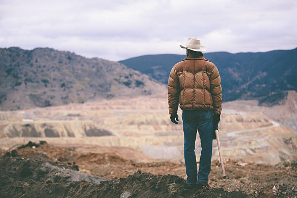 Man stands on mound of work site looking at mountains Man stands on dirt mound of work site looking at mountains rancher stock pictures, royalty-free photos & images