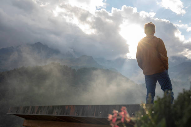 Man stands on rock tile roof and watches sun emerge from clouds stock photo