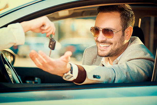 Man taking car key Handsome men sitting in a car at car dealership.He is receiving key from his new car. luxury car stock pictures, royalty-free photos & images