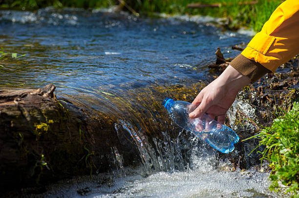man taking water from forest on hiking trip02 man taking bottle of water from a mountain stream. Enjoying the outdoors in the summer trekking vacation bushcraft stock pictures, royalty-free photos & images