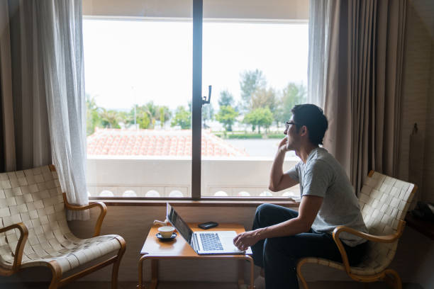 A man talking on a smart phone while looking out a hotel window stock photo