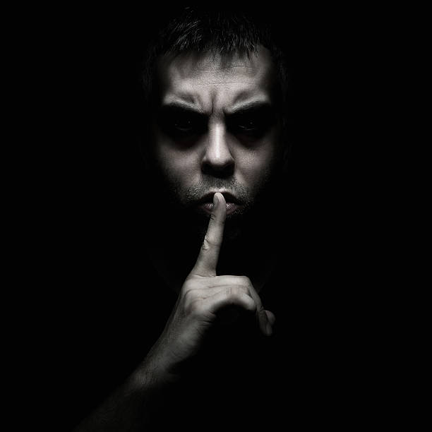 A man telling someone to be silent Evil man gesturing silence, quiet isolated on black background conspiracy stock pictures, royalty-free photos & images