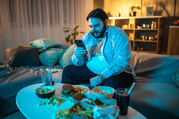Man text messaging on phone Cheerful man using mobile phone over the unhealthy food in living room fat man looks at the phone stock pictures, royalty-free photos & images