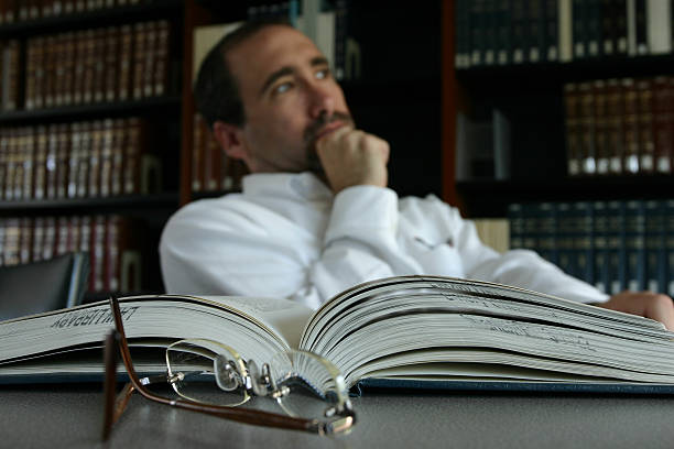 Man thinking at his desk by an open book in a library stock photo