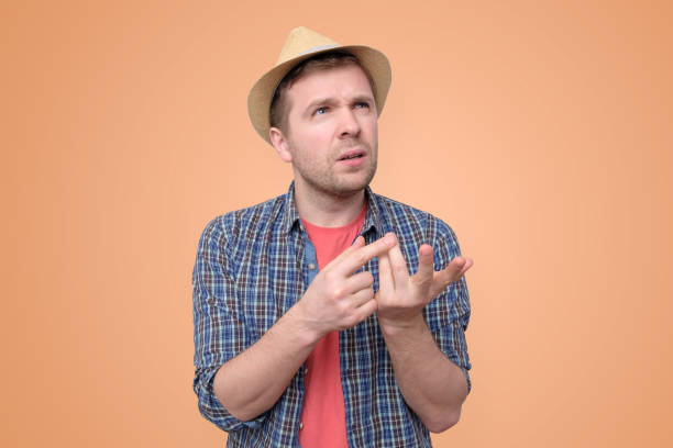 man thinking daydreaming trying hard to remember Young man in summer hat thinking daydreaming trying hard to remember something counting fingers, isolated on orange background. Negative emotion facial expressions feelings. counting stock pictures, royalty-free photos & images