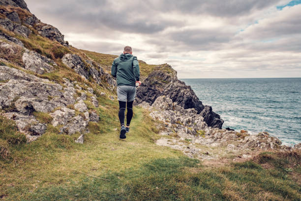 Man trail running along the rugged Cornish coastline on an Autumn day. stock photo
