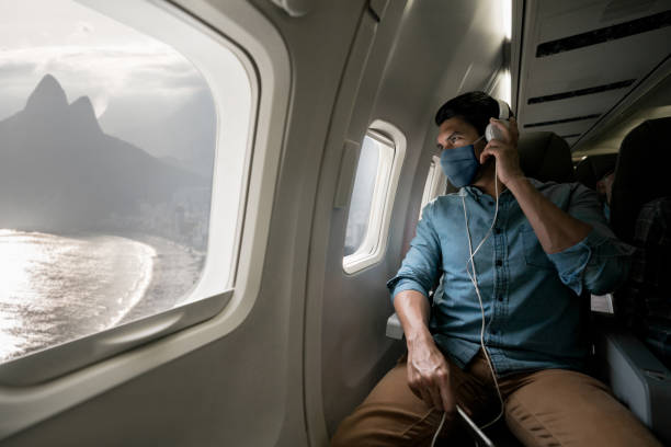 Man traveling by plane wearing a facemask and looking at Rio through the window Portrait of a Latin American man traveling by plane wearing a facemask during the COVID-19 pandemic and looking at Rio through the window plane window seat stock pictures, royalty-free photos & images