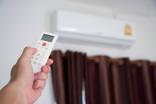 A man use remote controller to set air conditioner temperature in the room.Hand holdind control remote switch of home air conditioner stock photo