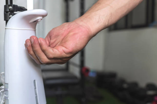 A man uses an automated hand sanitizer prior to entering a small gym. stock photo
