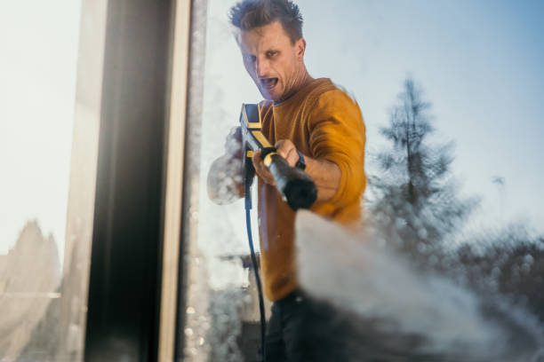 Man using a high pressure squirt gun to clean the window Man using a high pressure squirt gun to clean the window on sunny day. pressure washer stock pictures, royalty-free photos & images
